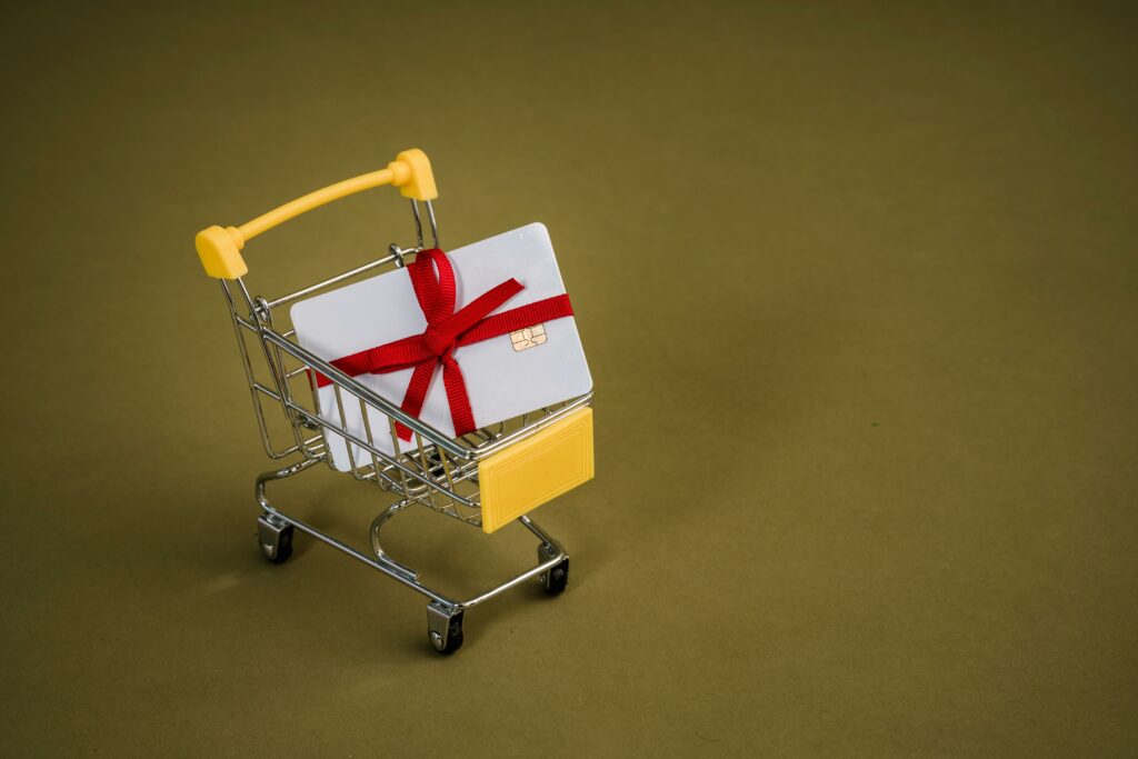 pexels photo 5926431 5926431 A gift card with a red bow sits in a mini shopping cart on a yellow backdrop.